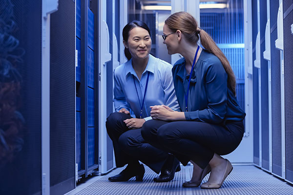 Two female engineers kneeling down and having a conversation in a data center